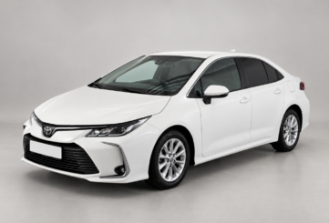 Белый седан Toyota Corolla на светлом фоне, вид спереди и сбоку.